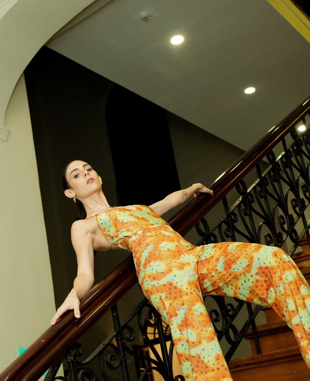 Modelo con mono de estampado naranja y verde apoyada en el barandal de hierro de la escalera del museo