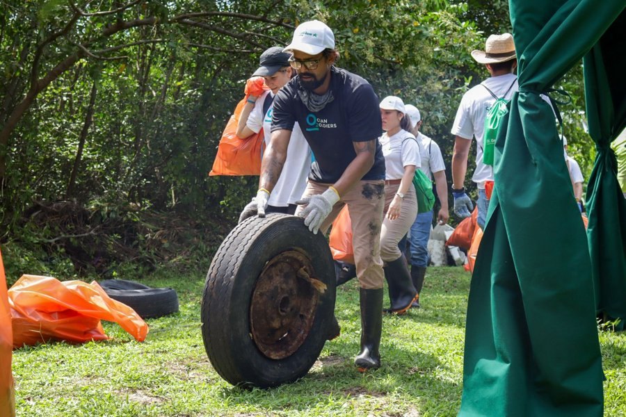Un voluntario rueda por el pasto un neumático con su llanta, recuperado durante la jornada de limpieza, mientras el resto del equipo traslada bolsas de residuos